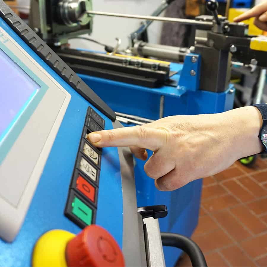 Eine Hand drückt einen Knopf auf einer Biegemaschine. Die Maschine ist blau mit unterschiedlich gefärbten Knöpfen.